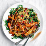 A plate full of roasted carrot salad with lentils, greens, and a tahini dressing on top.