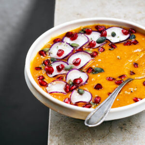A bowl of smooth orange soup with various toppings.
