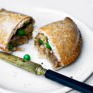 One half-moon pasty cut in half on a plate, with knife.