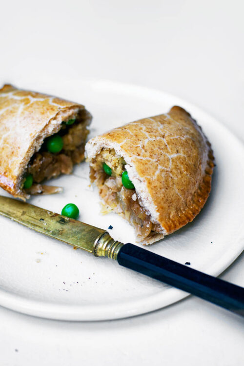 One half-moon pasty cut in half on a plate, with knife.