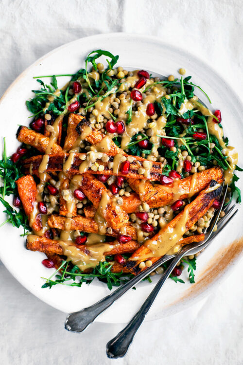 Roasted carrot lentil salad with arugula and tahini sauce on white plate.