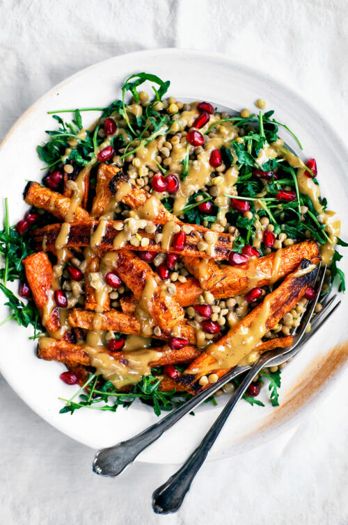 Roasted carrot lentil salad with arugula and tahini sauce on white plate.