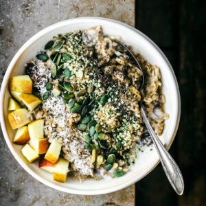 Apple porridge in a bowl on a ledge with fruit and seed toppings.