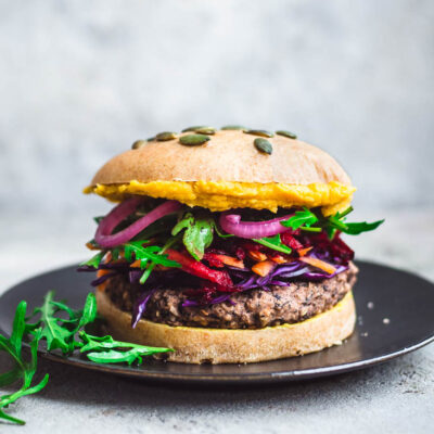 A black bean burger on a plate with vegetable toppings.