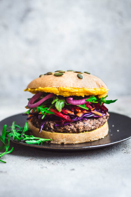 A black bean burger on a plate with vegetable toppings.