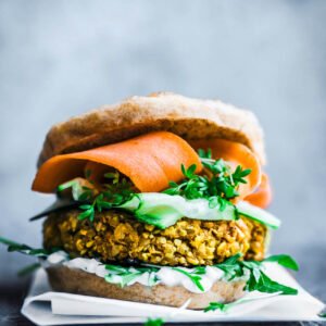 A yellow cauliflower burger patty in a bun with greens and carrot slices.