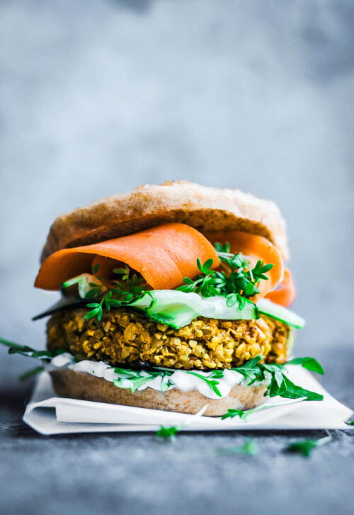 A yellow cauliflower burger patty in a bun with greens and carrot slices.