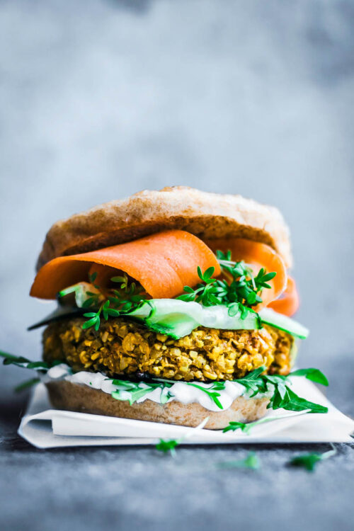 A yellow cauliflower burger patty in a bun with greens and carrot slices.