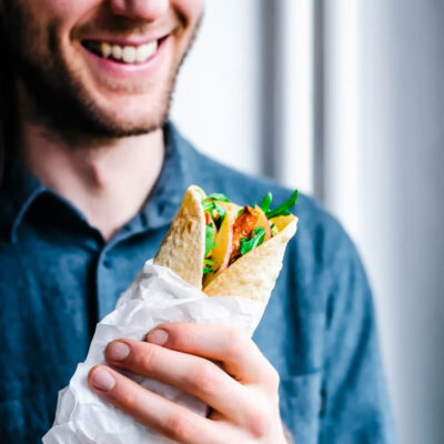 Man holding a wrap filled with vegetables and greens.