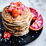 A stack of pancakes topped with orange pieces and coconut.