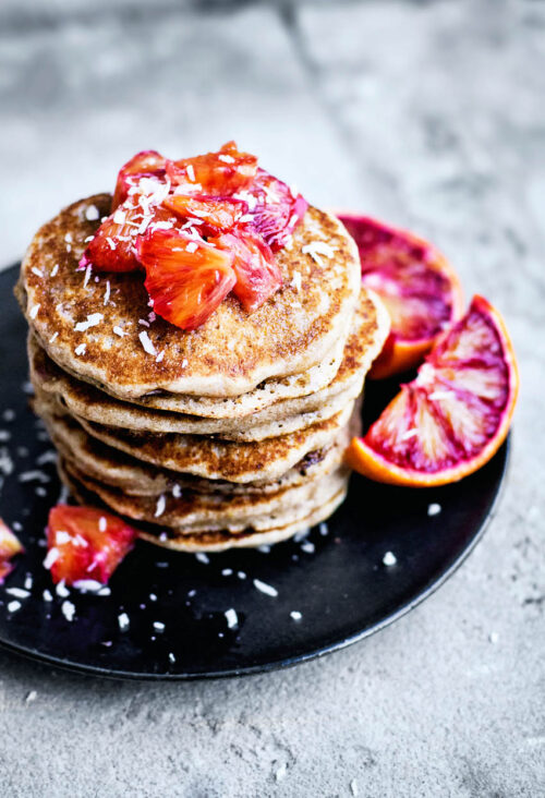 A stack of pancakes topped with orange pieces and coconut.