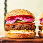 Close up of two black bean burgers on buns with various burger toppings.