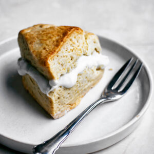 A triangular scone filled with cream on a small plate with a fork.