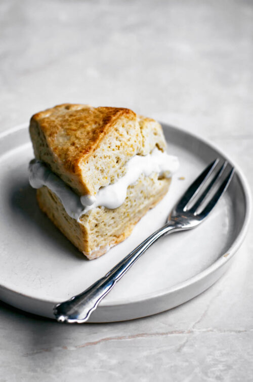 A triangular scone filled with cream on a small plate with a fork.
