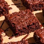 Brownies cut into squares with extra chocolate drizzled on top.