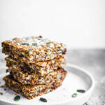 A stack of four carrot and seed granola bars on a small plate.