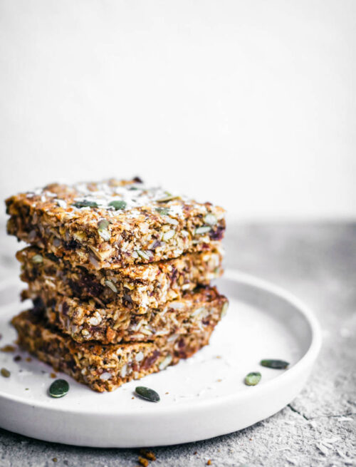 A stack of four carrot and seed granola bars on a small plate.