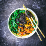 A vegetable noodle curry in a white bowl with chopsticks.