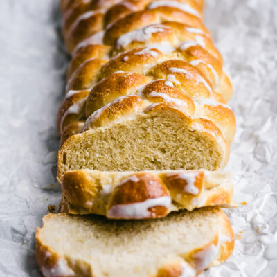 Six strand challah, front view, on parchment paper with icing drizzle, two slices cut at front