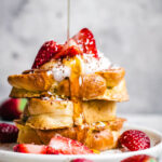 Stack of three pieces of challah french toast, with strawberries and maple syrup.