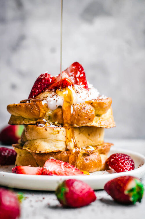 Stack of three pieces of challah french toast, with strawberries and maple syrup.