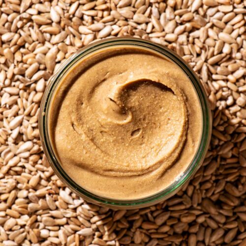 A glass jar of seed butter resting on sunflower seeds.