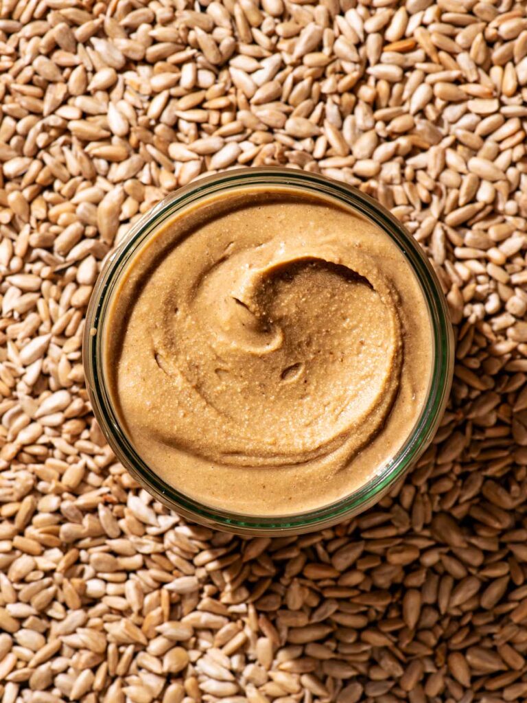 A glass jar of seed butter resting on sunflower seeds.