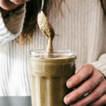 Woman holding a jar of seed butter and lifting a spoonful out.