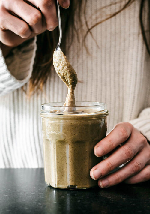Woman holding a jar of seed butter and lifting a spoonful out.