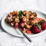 Strawberry rhubarb crisp on plate with fresh berries.