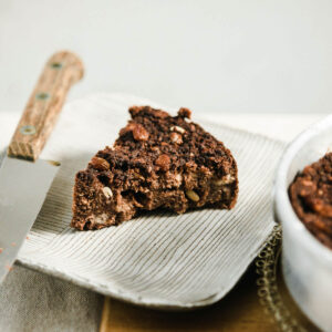A slice of chocolate bread pudding with nuts and raisins on a plate.