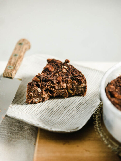 A slice of chocolate bread pudding with nuts and raisins on a plate.