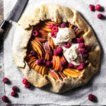 A peach and apricot galette with ice cream and raspberries on parchment paper.