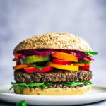 Close up of a bean burger topped with summer vegetables.