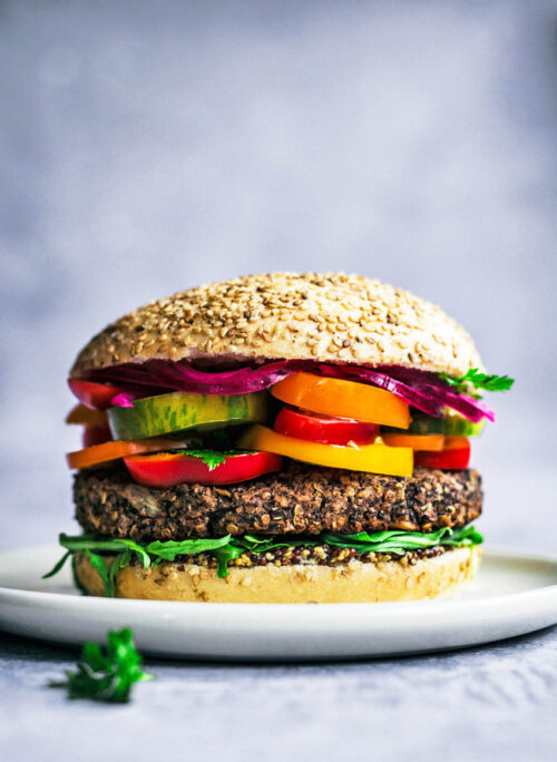 Close up of a bean burger topped with summer vegetables.