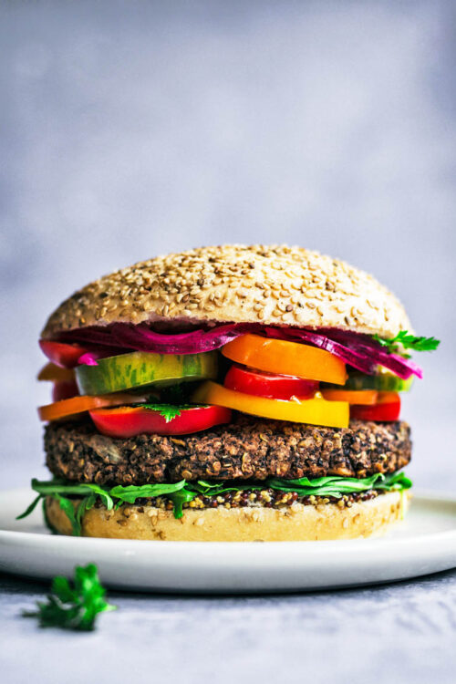 Close up of a bean burger topped with summer vegetables.