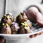 Woman holding a plate with date truffles, each topped with chocolate and nuts.