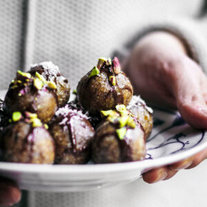Woman holding a plate with date truffles, each topped with chocolate and nuts.