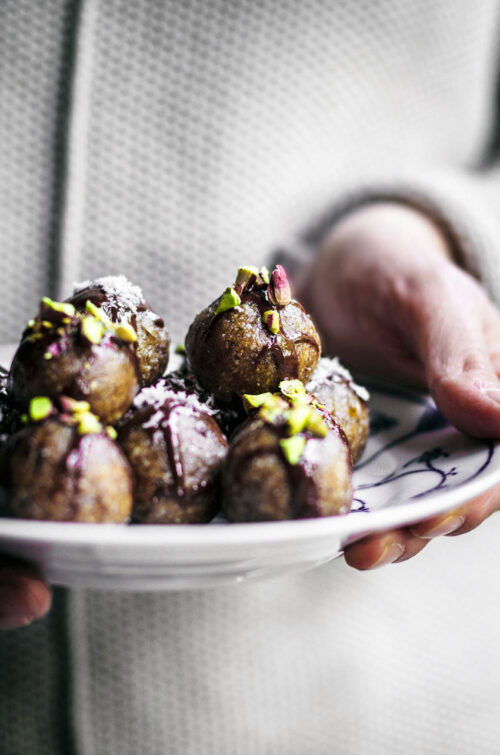Woman holding a plate with date truffles, each topped with chocolate and nuts.