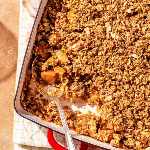 Oat apple crisp in a red metal baking dish, with a scoop removed.