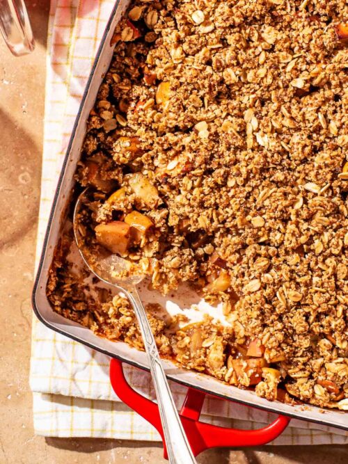 Oat apple crisp in a red metal baking dish, with a scoop removed.