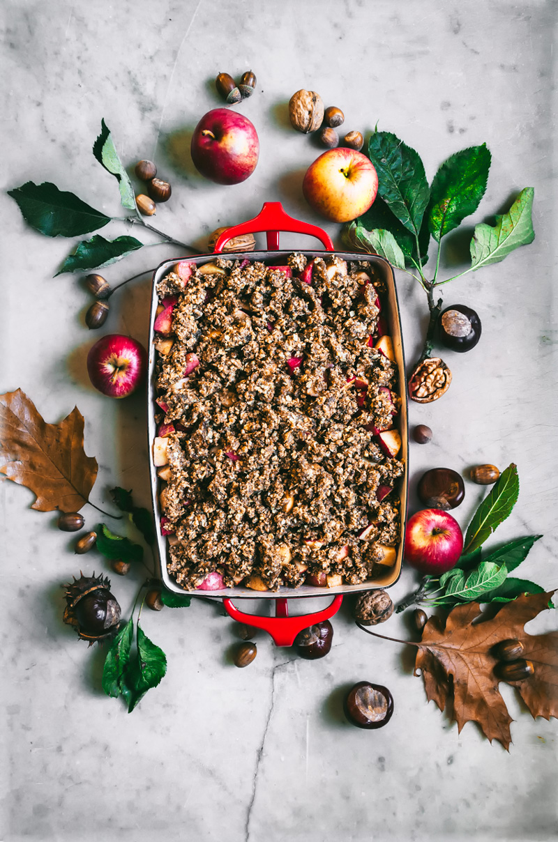 Hazelnut apple crumble in baking dish, surrounded by autumn leaves, unbaked.