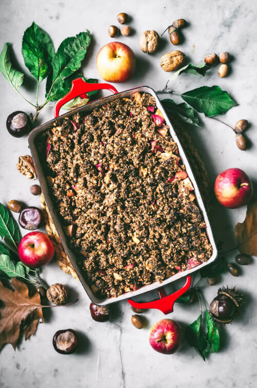 Apple crumble in a baking dish with autumn foliage around.