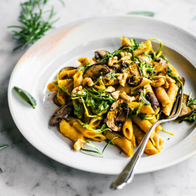 A plate of pasta with pumpkin sauce, mushrooms, and greens.