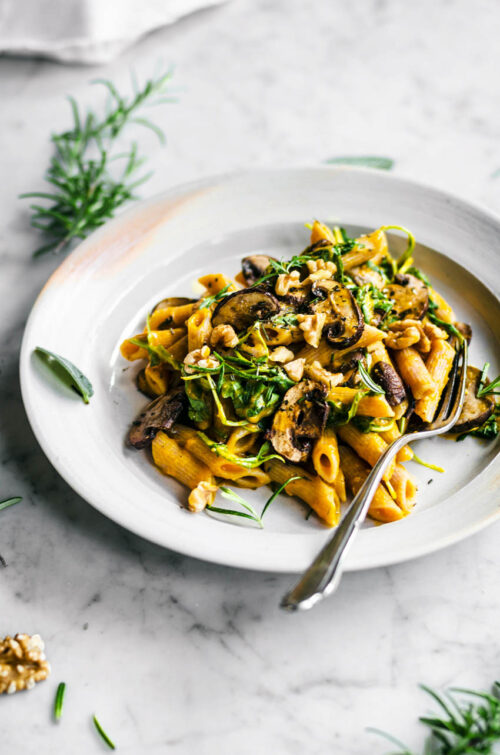 A plate of pasta with pumpkin sauce, mushrooms, and greens.