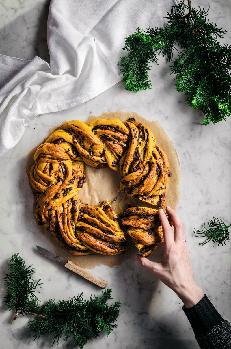 yellow saffron braided wreath bread with chocolate, on marble backdrop with hands holding a slice