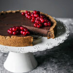 Ganache filled tart topped with red currants, one slice removed.