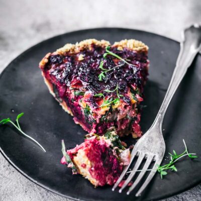 Beet tart slice on black plate, with fork and one bite cut.
