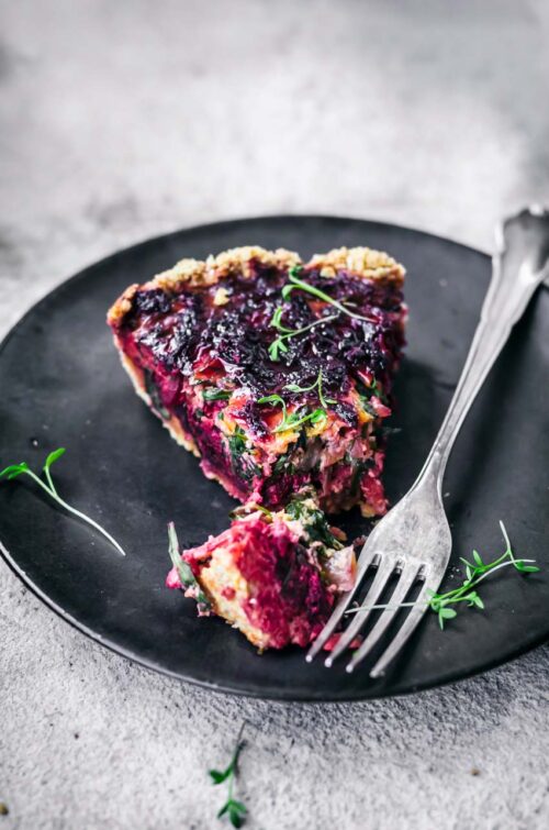 Beet tart slice on black plate, with fork and one bite cut.