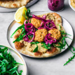 Three lentil falafel on a piece of naan with hummus, greens, and pickled onions.